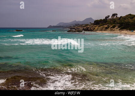 Vue sur la plage de Cala Ratjada avec du sable, des rochers et des montagnes en arrière-plan sur l'île des Baléares Mallorca, Espagne sur une journée ensoleillée avec des turquo Banque D'Images