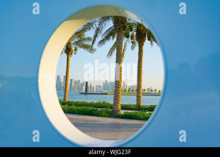 Le long de la Corniche vue de Doha, quartier des affaires de grande hauteur par trou circulaire avec trois palmiers et port. Banque D'Images