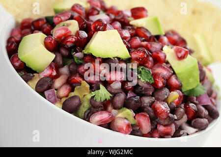 Un sain ou relish salsa avec grenade, avocat, oignons rouges, haricots noirs et de coriandre servi avec des chips de maïs. Banque D'Images