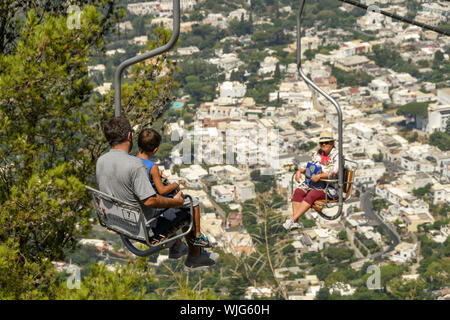 ANACAPRI, à l'île de Capri, ITALIE - AOÛT 2019 : les gens sur un télésiège monte ou descend le long de la montagne jusqu'au sommet du Mont Solaro, Anacapri ci-dessus Banque D'Images