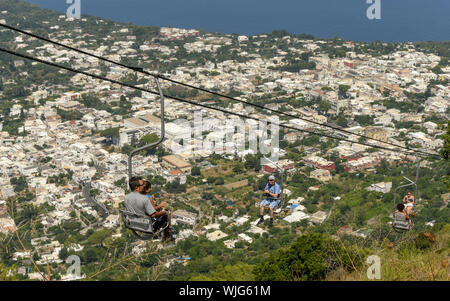 ANACAPRI, à l'île de Capri, ITALIE - AOÛT 2019 : les gens sur un télésiège monte ou descend le long de la montagne jusqu'au sommet du Mont Solaro, Anacapri ci-dessus Banque D'Images