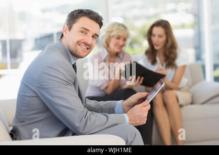 Businessman using digital tablet avec collègues femmes assis sur le canapé en arrière-plan à la maison Banque D'Images