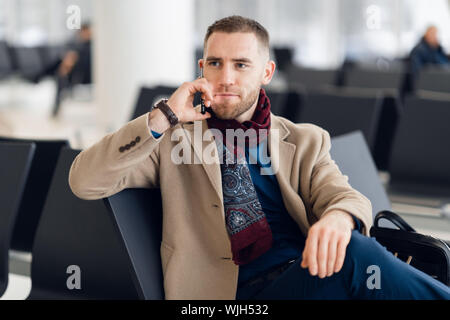 Jeune homme sérieux wearing scarf et coat talking on mobile phone close-up Banque D'Images