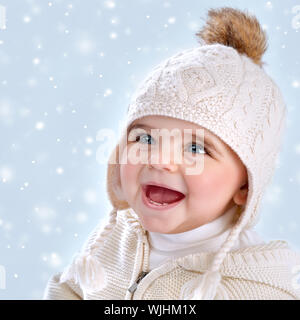 Closeup portrait of cute little baby girl wearing hat élégant chaud isolé sur fond de neige bleu, chute de neige, hiver, concept enfant heureux Banque D'Images