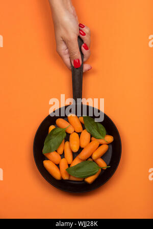 Carotte bébé sur la poêle. Isolé sur orange. Banque D'Images