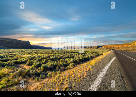 Bien que la longue route qui serpente dans le désert des terres de brosse plate dans les montagnes de l'intérieur des terres au nord-ouest de l'État de Washington rural dans le désert américain Banque D'Images