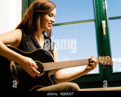 Photo d'une femme dans sa fin des années 20 à l'affiche une guitare acoustique par une grande fenêtre. Banque D'Images