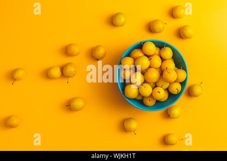 Modèle d'été créatif à base de produits frais dans les prunes cerises jaunes bol bleu sur fond jaune pastel. Concept minimal de fruits. Mise à plat. Banque D'Images