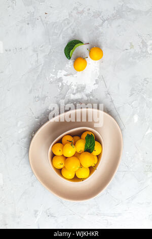 Modèle d'été créatif à base de produits frais dans les prunes cerises jaunes bol rose sur fond de béton gris. Concept minimal de fruits. Mise à plat. Banque D'Images