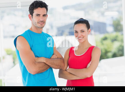 Portrait d'un jeune couple fit debout avec les bras croisés dans une salle d'exercice lumineux Banque D'Images