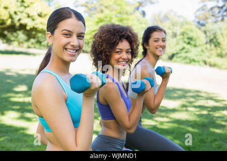 Side view portrait of smiling woman lifting dumbbells in park Banque D'Images