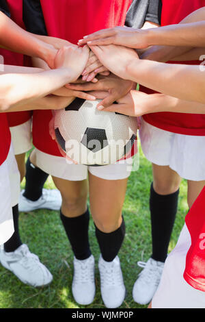 Portrait de l'équipe de soccer féminin des mains d'empilage sur ball at park Banque D'Images