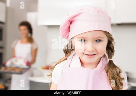 Petite fille portant un tablier rose et chefs hat smiling at camera à la maison dans la cuisine Banque D'Images