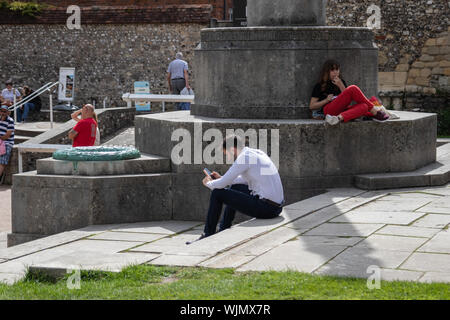 Un homme d'affaires dans l'habillement assis sur les marches d'un monument commémoratif de guerre à l'aide de son téléphone mobile ou téléphone cellulaire sur sa pause déjeuner Banque D'Images