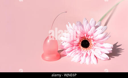 Coupe menstruelle et fleur rose sur fond rose. Banque D'Images