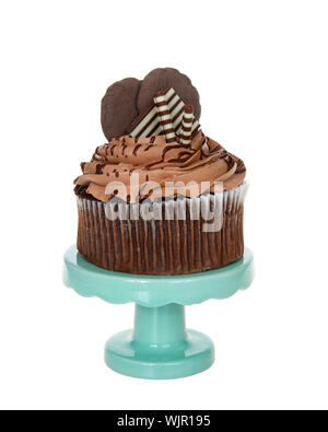 Cup cake au chocolat géant avec glaçage au chocolat, bonbons et biscuits de rehaussement assis sur un piédestal vert sarcelle isolé sur blanc. Banque D'Images