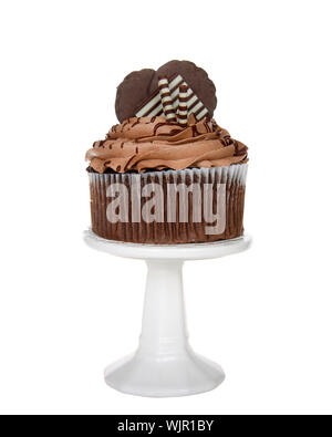 Cup cake au chocolat géant avec glaçage au chocolat, bonbons et biscuits de rehaussement assis sur un piédestal blanc isolé sur blanc. Banque D'Images