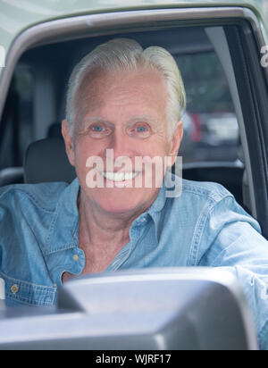 Un joli Happy Senior Man tourné en tête d'âge de 70 La fenêtre d'une voiture souriant à l'appareil photo avec des cheveux blancs et est relâché. Banque D'Images
