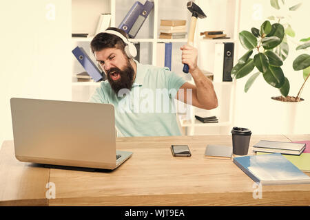 Homme barbu bureau écouteurs swing marteau sur ordinateur. Connexion internet lente. Logiciel obsolète. Décalage de l'ordinateur. Pour des raisons du retard de l'ordinateur. Comment fixer la traîne lente du système. La routine du bureau. Banque D'Images