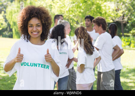 Portrait of female volunteer showing Thumbs up avec des amis en arrière-plan disucssing Banque D'Images