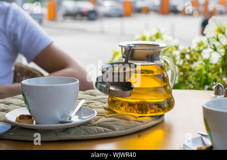 Thé infusé dans une théière sur une table dans un café en plein air sur l'arrière-plan de tasses à thé, téléphone portable, porte-monnaie et un homme assis à une table Banque D'Images