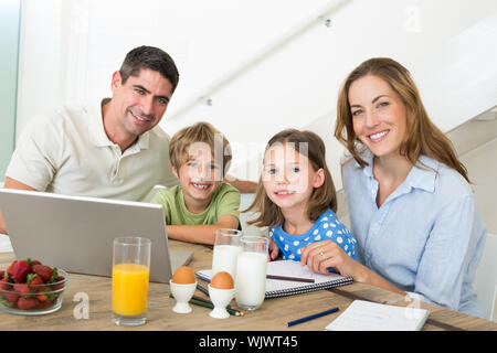 Portrait of smiling family using laptop pendant le petit-déjeuner à la maison Banque D'Images