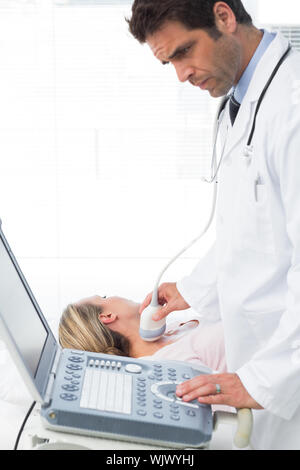 Médecin homme concentré sur le cou de l'aide de sonogramme female patient in examination room Banque D'Images