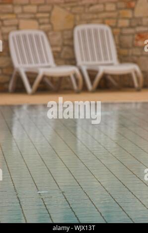 Sièges en plastique blanc debout sur une terrasse à côté d'une piscine Banque D'Images