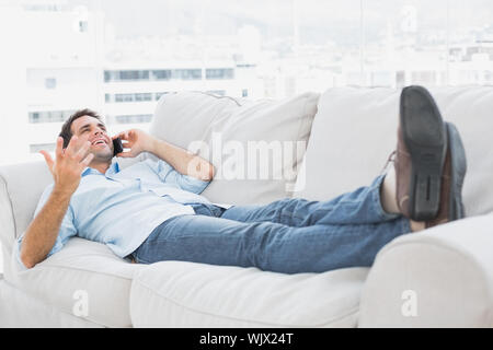 Smiling man allongé sur le canapé à parler au téléphone à la maison dans le salon Banque D'Images