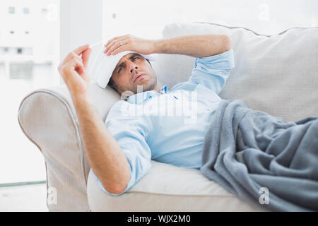 Sick man contrôler sa température sous une couverture à la maison dans le salon Banque D'Images