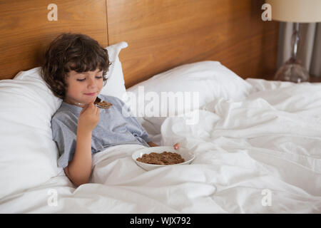 Smiling Young boy eating breakfast in bed at home Banque D'Images