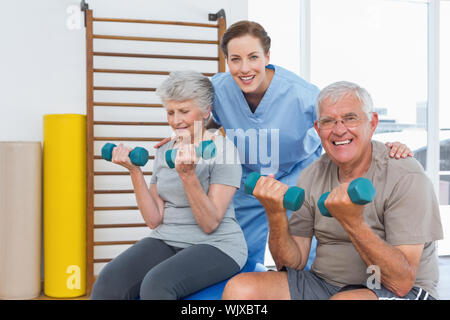 Female therapist aider senior couple with dumbbells dans le bureau médical Banque D'Images