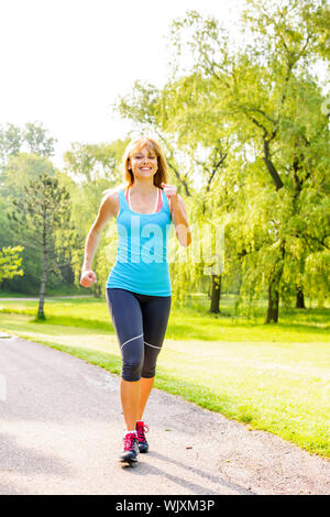 Smiling woman exercising on sentier de jogging dans le parc d'été vert Banque D'Images