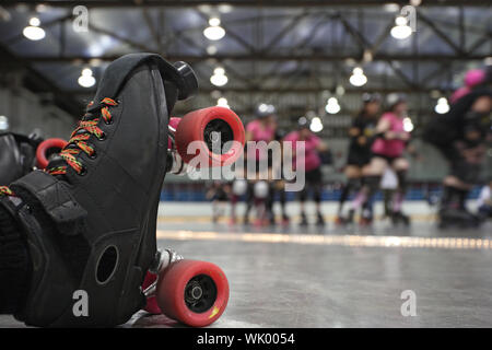 Une image abstraite du patins à roulettes d'un patineur tombé comme ses coéquipières dans le fond continuer à patiner autour de la piste du roller derby. Banque D'Images