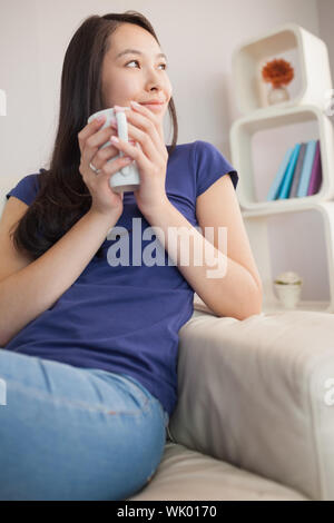 Young Asian woman sitting on the couch holding mug Banque D'Images