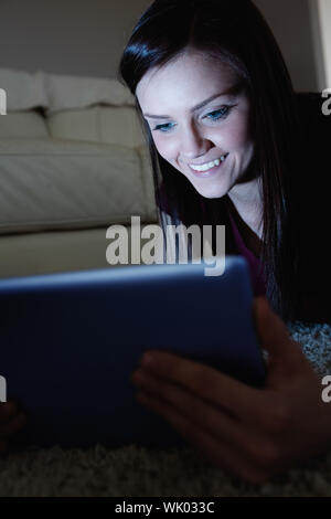 Smiling brunette lying on floor using tablet pc dans le noir Banque D'Images