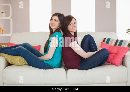 Deux smiling friends assis dos à dos sur le canapé Banque D'Images