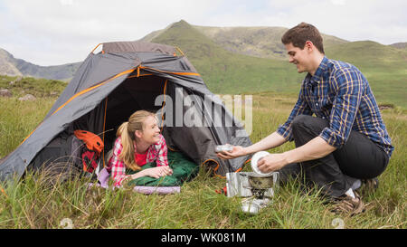 Smiling couple cooking outside on camping trip Banque D'Images