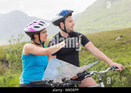 Couple on mountain bikes holding map and pointing Banque D'Images