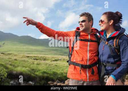 Couple wearing rain jackets and sunglasses admirant le paysage avec homme pointant Banque D'Images