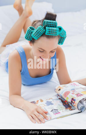 Smiling girl in hair rollers lying on bed Banque D'Images