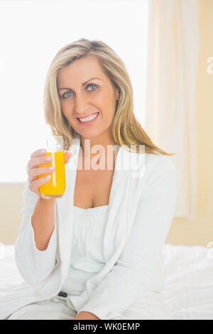 Femme joyeuse à la caméra en buvant un verre de jus d'orange Banque D'Images