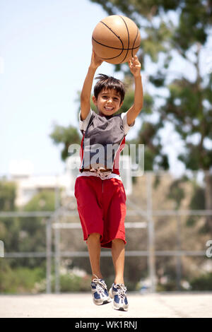 Jeune joueur de basket-ball haut saut dans l'air comme il jette le ballon Banque D'Images