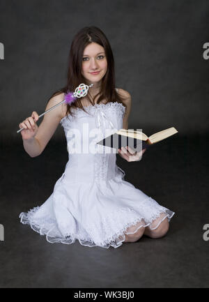 Fille - fée dans une robe blanche avec une baguette magique et le livre sur un fond noir Banque D'Images