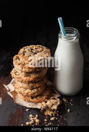 Biscuits bio faits maison avec des raisins et des abricots et bouteille de lait sur fond de bois sombre. Banque D'Images