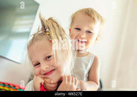 Cute blonde caucaian adorable petite soeur l'étreindre tout-petit frère.Couple de frère joyeux jouant à l'intérieur. Jolie fille et garçon bébé profiter Banque D'Images