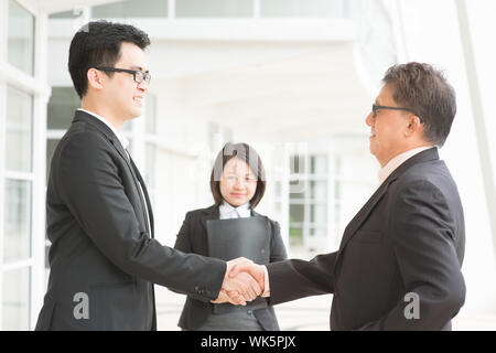 Transaction commerciale, d'affaires de l'Asie l'établissement de liaison. Chef principal part agiter avec de jeunes dirigeants. Immeuble de bureaux moderne architecture. Banque D'Images