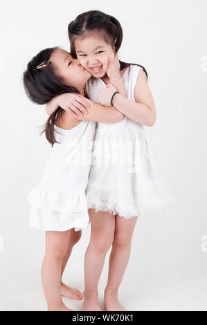 Les petites filles portrait. Asian sisters, baiser sur fond uni. Amour d'enfant. Banque D'Images
