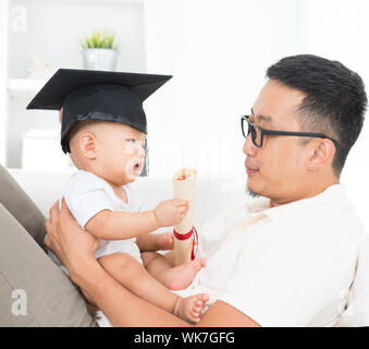 Vie de famille asiatique à la maison. Bébé avec graduation cap holding certificat. Père de l'enfant et l'éducation précoce concept. Banque D'Images