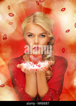 Jolie femme en robe rouge blowing kisses sur les paumes des mains Banque D'Images